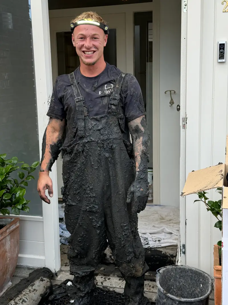 Medewerker van PuinVrij in een werkoverall vol modder, net uit de kruipruimte