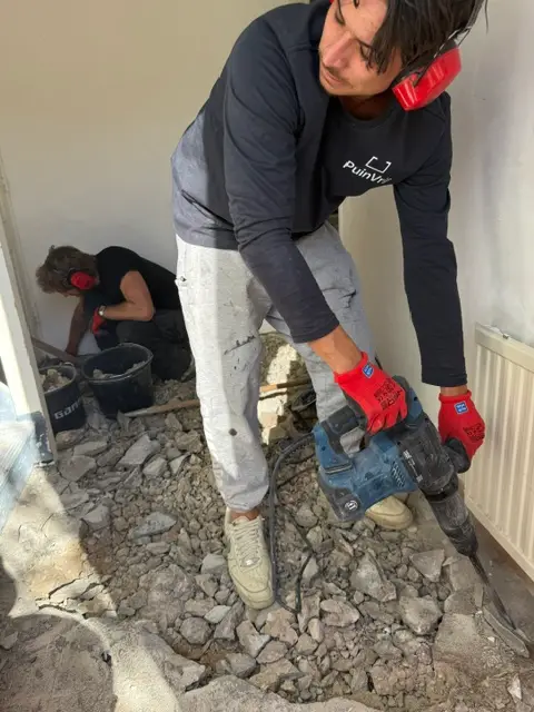 Medewerker van PuinVrij met gehoorbescherming breekt een tegelvloer in een hal op met een breekhamer
