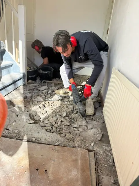 Twee medewerkers van PuinVrij met gehoorbescherming breken de tegelvloer van een hal op