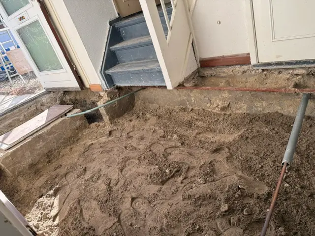 Dezelfde hal na het slopen: de vloer is eruit en er ligt een vlakke zandbodem voor de trap